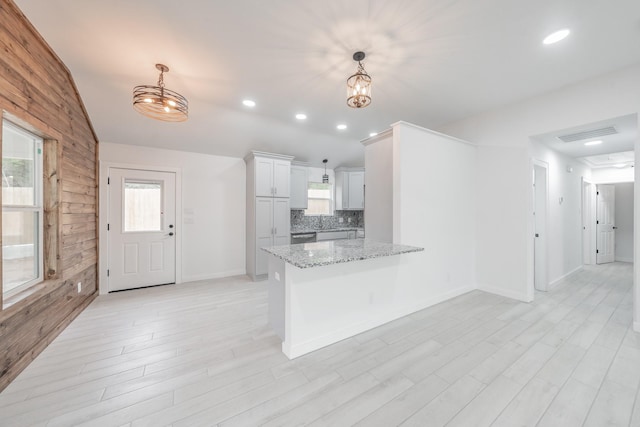 kitchen with kitchen peninsula, decorative backsplash, a notable chandelier, pendant lighting, and light stone counters