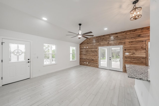 entryway featuring wooden walls, lofted ceiling, french doors, ceiling fan with notable chandelier, and light hardwood / wood-style flooring