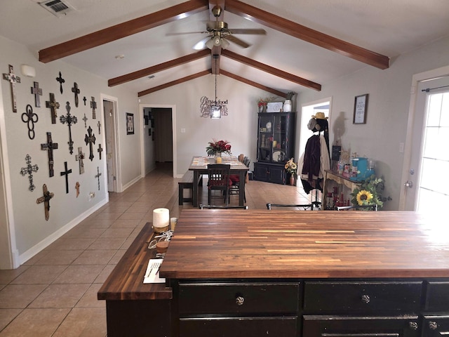 interior space featuring light tile patterned flooring, ceiling fan with notable chandelier, wooden counters, and lofted ceiling with beams