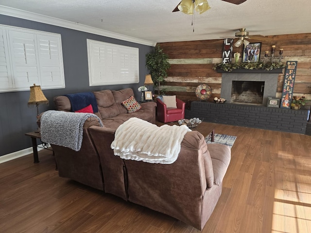 living room with wooden walls, a brick fireplace, wood-type flooring, a textured ceiling, and ornamental molding