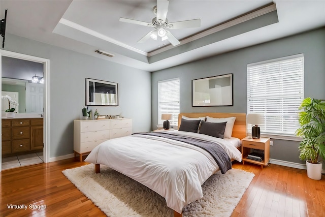 bedroom with ceiling fan, ensuite bathroom, a raised ceiling, light wood-type flooring, and ornamental molding