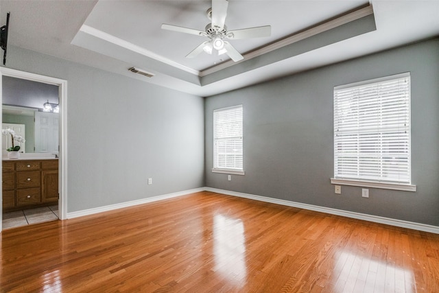 unfurnished bedroom with ceiling fan, light hardwood / wood-style floors, connected bathroom, and a raised ceiling