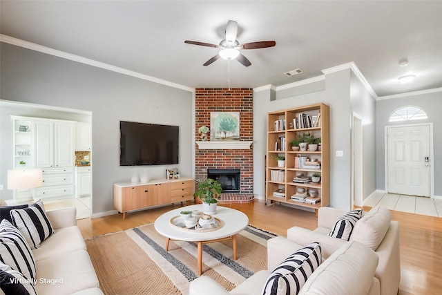 living room featuring light wood-type flooring, a brick fireplace, crown molding, and ceiling fan