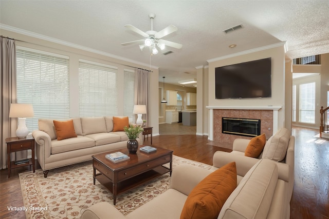 living room featuring crown molding, a tiled fireplace, ceiling fan, a textured ceiling, and wood finished floors