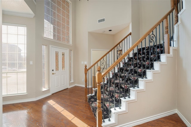 foyer entrance with wood-type flooring, a high ceiling, and ornamental molding