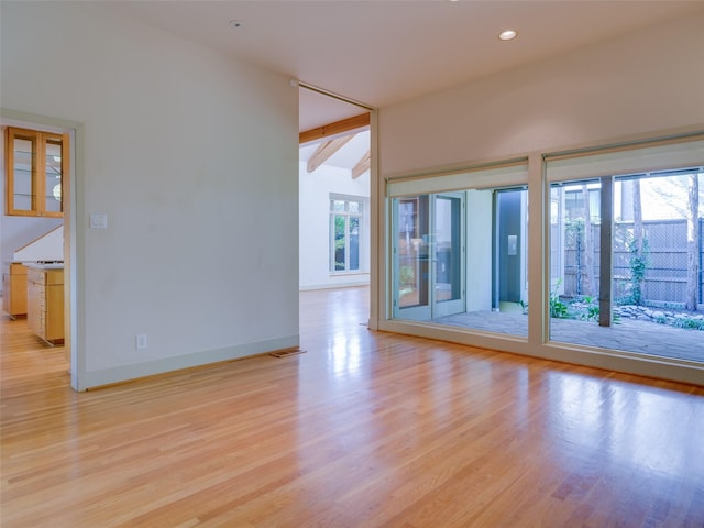 unfurnished room featuring light hardwood / wood-style floors and vaulted ceiling with beams