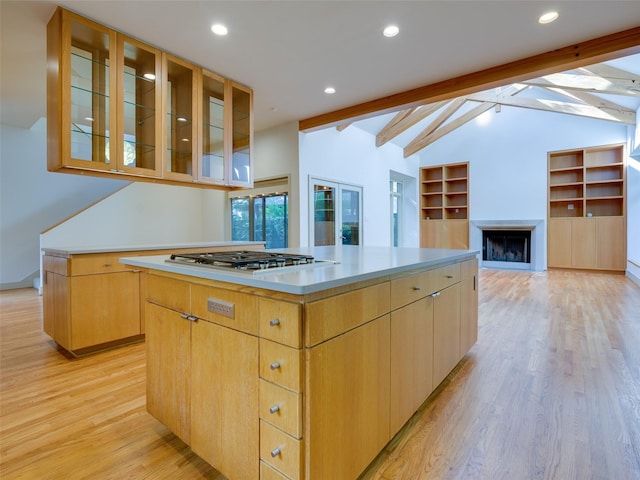 kitchen with stainless steel gas stovetop, a center island, light brown cabinetry, light hardwood / wood-style flooring, and lofted ceiling with beams