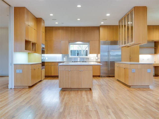 kitchen with stainless steel appliances, a center island, light wood-type flooring, light brown cabinetry, and sink