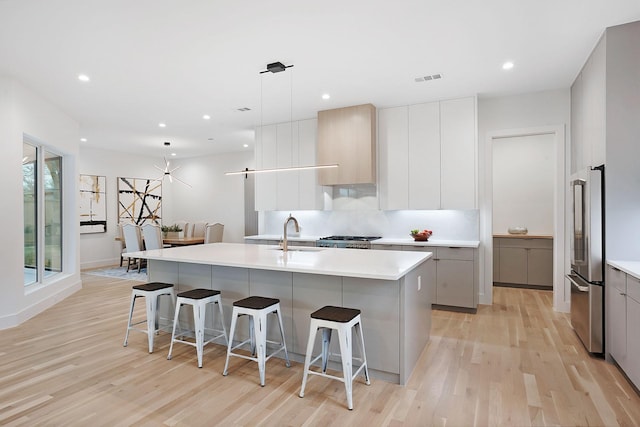 kitchen with hanging light fixtures, a kitchen island with sink, stainless steel fridge, and sink