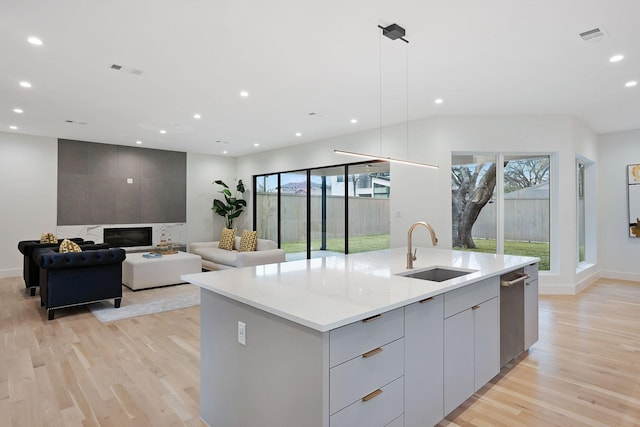 kitchen with a center island with sink, gray cabinets, decorative light fixtures, a fireplace, and sink