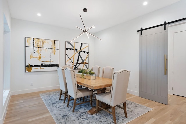 dining space with a barn door, a chandelier, and light hardwood / wood-style flooring