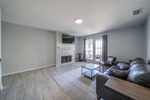 living room featuring light hardwood / wood-style floors, french doors, and a tiled fireplace