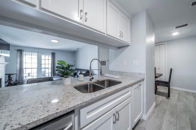 kitchen with white cabinets, dishwasher, sink, light wood-type flooring, and light stone counters