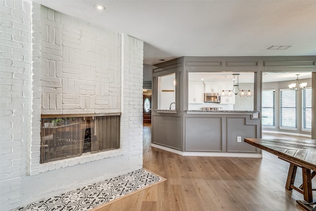 kitchen featuring decorative light fixtures, a brick fireplace, kitchen peninsula, hardwood / wood-style flooring, and a chandelier