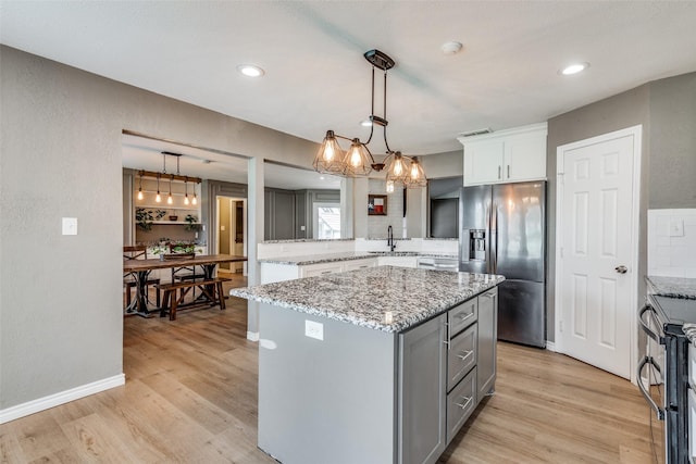 kitchen featuring appliances with stainless steel finishes, a center island, light hardwood / wood-style floors, sink, and hanging light fixtures