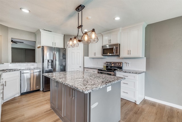 kitchen featuring stainless steel appliances, white cabinets, decorative light fixtures, and a center island