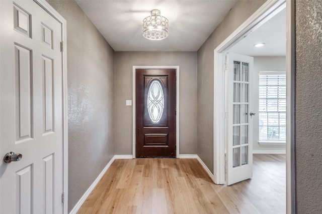 entryway with a textured ceiling, light hardwood / wood-style flooring, and a notable chandelier