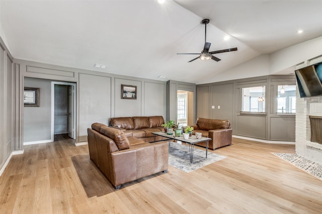 living room with ceiling fan, lofted ceiling, a brick fireplace, and light hardwood / wood-style floors