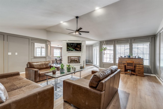 living room featuring ceiling fan, vaulted ceiling, a fireplace, and light hardwood / wood-style flooring