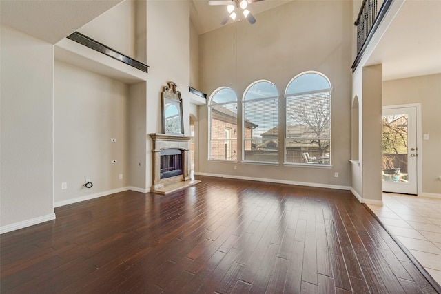 unfurnished living room with ceiling fan, dark wood-type flooring, a wealth of natural light, and a towering ceiling