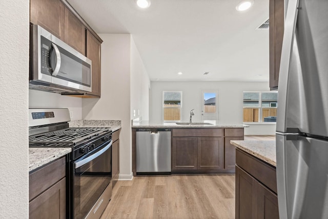 kitchen with appliances with stainless steel finishes, sink, light stone counters, and plenty of natural light