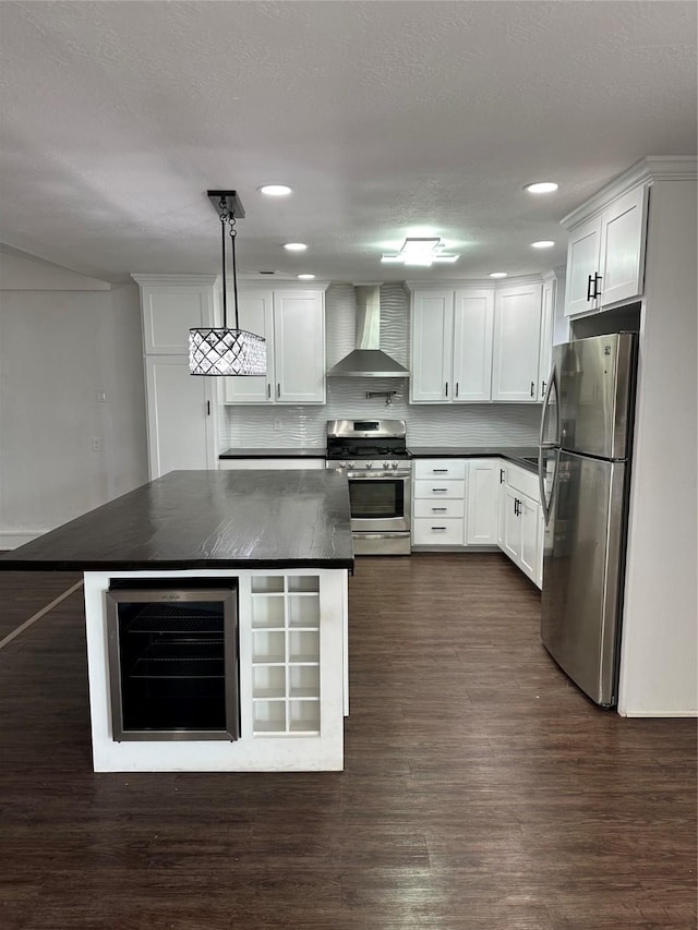 kitchen with stainless steel appliances, beverage cooler, wall chimney range hood, pendant lighting, and white cabinets