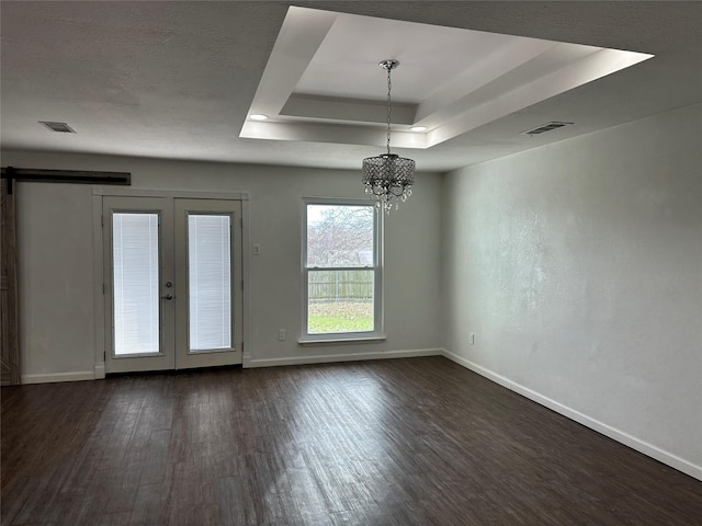 spare room featuring a barn door, a notable chandelier, a raised ceiling, dark wood-type flooring, and french doors