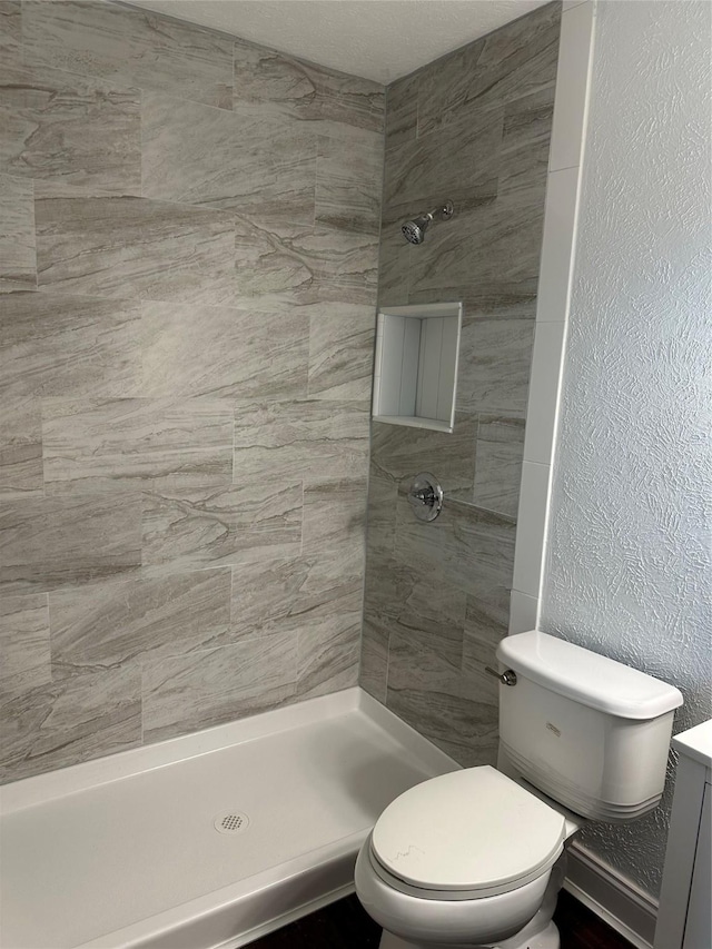 bathroom with toilet, tiled shower, and vanity