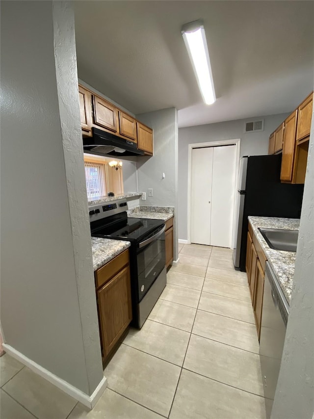 kitchen with light tile patterned floors, stainless steel appliances, light stone counters, and sink