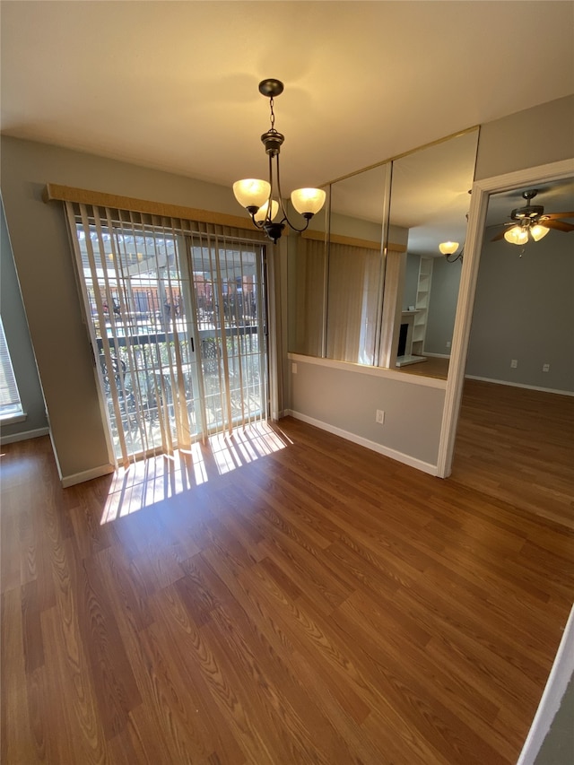 unfurnished dining area featuring dark hardwood / wood-style flooring, a wealth of natural light, and ceiling fan with notable chandelier