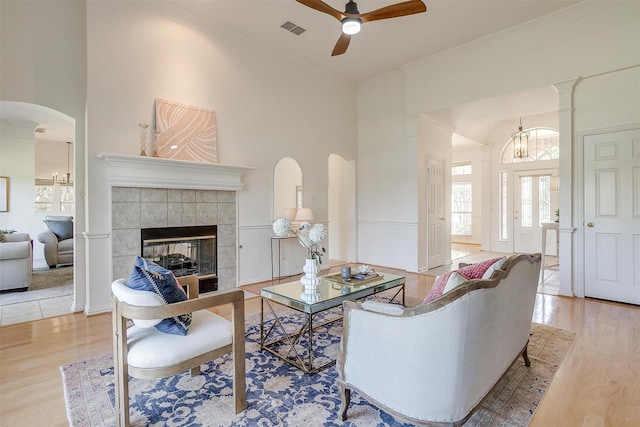 living room featuring ceiling fan, a towering ceiling, a tile fireplace, and light hardwood / wood-style floors