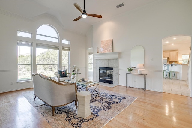 living room with light wood-type flooring, ceiling fan, a tile fireplace, and high vaulted ceiling