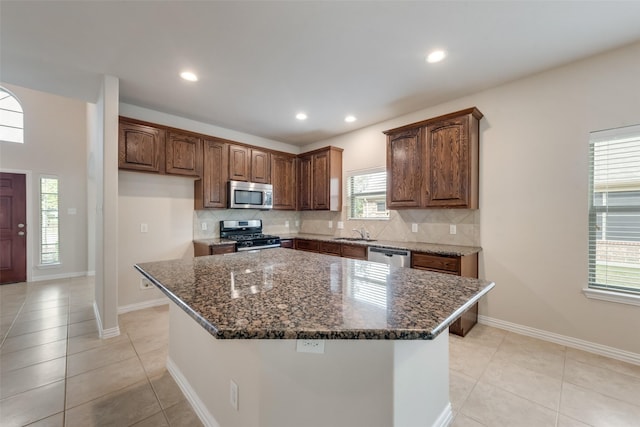 kitchen featuring appliances with stainless steel finishes, a kitchen island, dark stone counters, tasteful backsplash, and light tile patterned floors