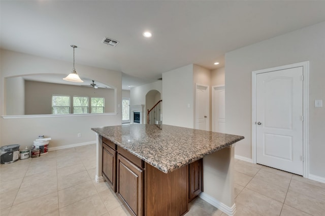 kitchen with light tile patterned floors, ceiling fan, hanging light fixtures, stone counters, and a center island