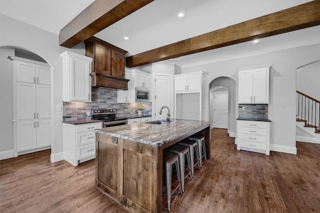 kitchen featuring a center island with sink, stainless steel appliances, beam ceiling, white cabinets, and sink