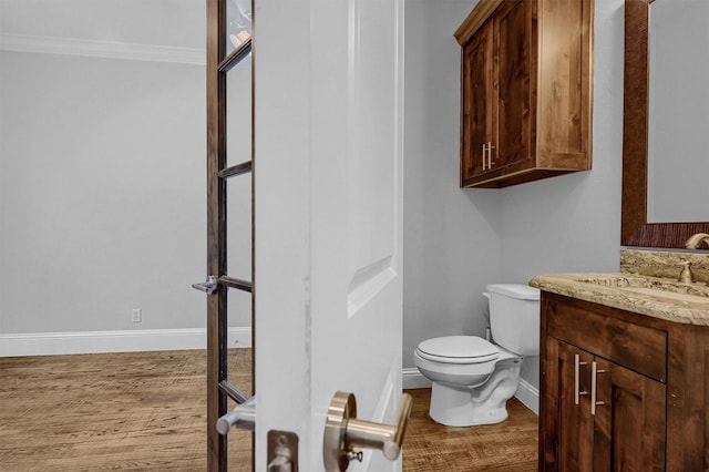 bathroom featuring baseboards, wood finished floors, toilet, and crown molding