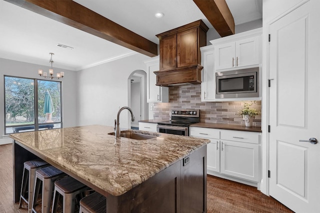 kitchen with white cabinetry, stainless steel appliances, sink, a center island with sink, and beam ceiling