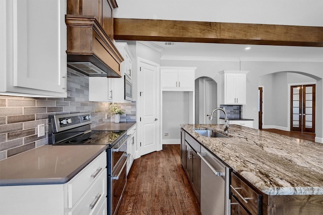 kitchen featuring arched walkways, a sink, appliances with stainless steel finishes, dark stone counters, and dark wood finished floors