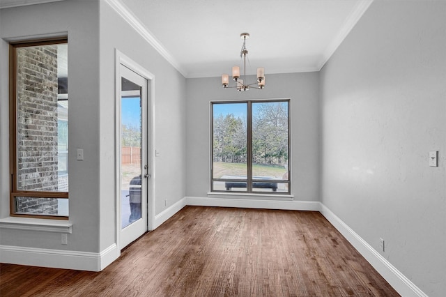 unfurnished dining area with a chandelier, baseboards, wood finished floors, and crown molding