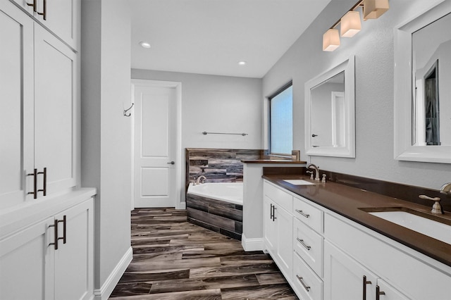 bathroom featuring double vanity, a garden tub, a sink, and wood finished floors