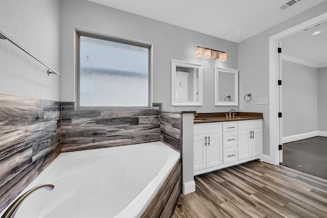 bathroom featuring a garden tub, a sink, wood finished floors, visible vents, and double vanity