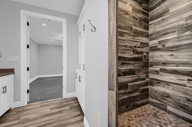 full bathroom with tiled shower, vanity, baseboards, and wood finished floors