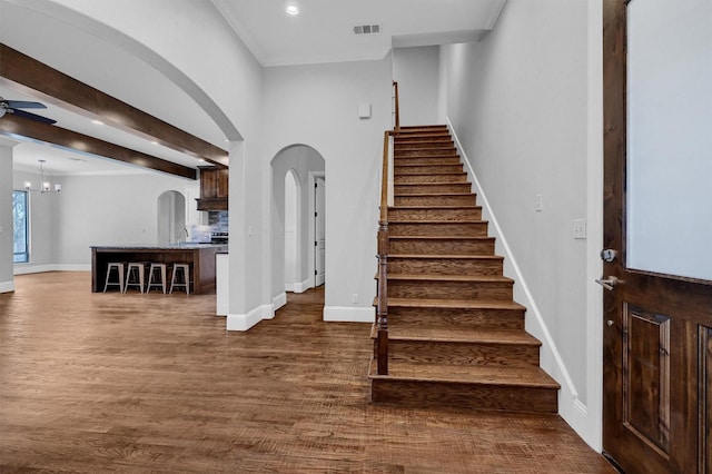 stairway featuring arched walkways, ceiling fan with notable chandelier, wood finished floors, and visible vents