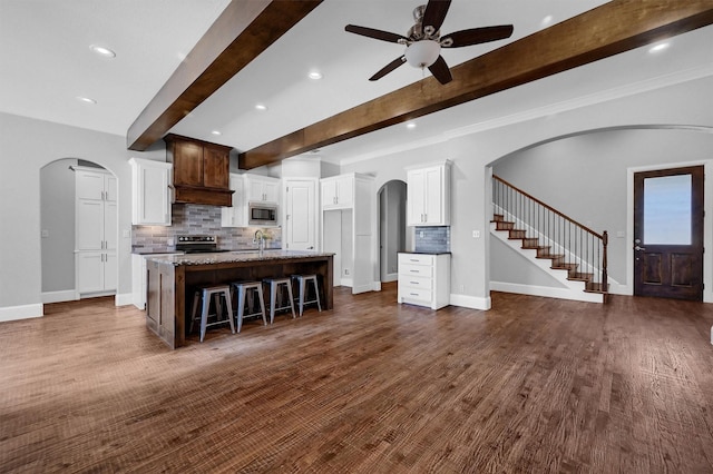 kitchen with stone counters, beamed ceiling, appliances with stainless steel finishes, an island with sink, and a breakfast bar area