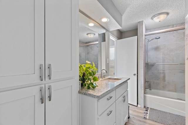 bathroom featuring a textured ceiling, bath / shower combo with glass door, wood-type flooring, and vanity