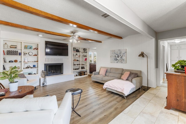 living room featuring ceiling fan, light hardwood / wood-style floors, beam ceiling, a large fireplace, and a textured ceiling