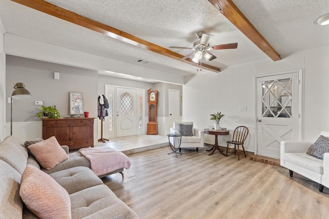 living room with ceiling fan, a textured ceiling, light hardwood / wood-style flooring, and beam ceiling