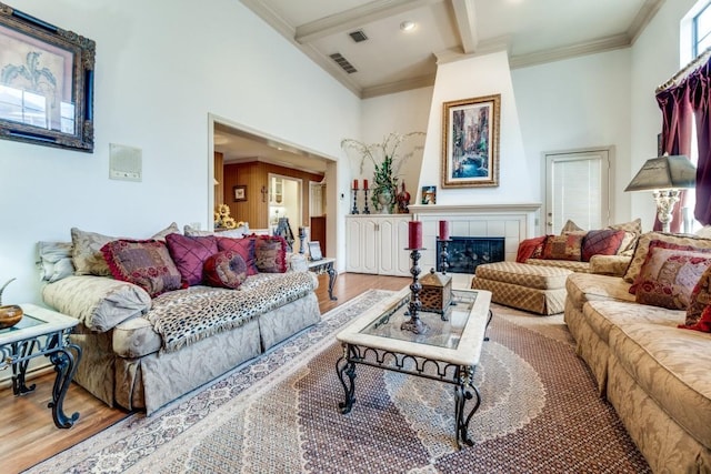 living room with hardwood / wood-style flooring, a tile fireplace, crown molding, and beamed ceiling