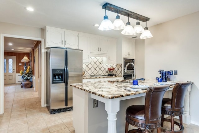 kitchen with tasteful backsplash, hanging light fixtures, light stone countertops, appliances with stainless steel finishes, and white cabinets