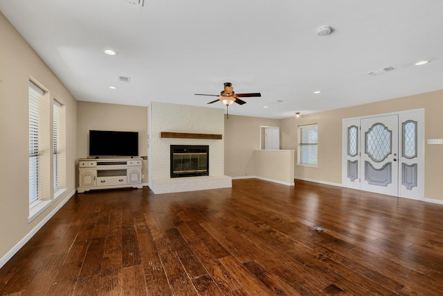 unfurnished living room with dark wood-type flooring, a brick fireplace, plenty of natural light, and ceiling fan